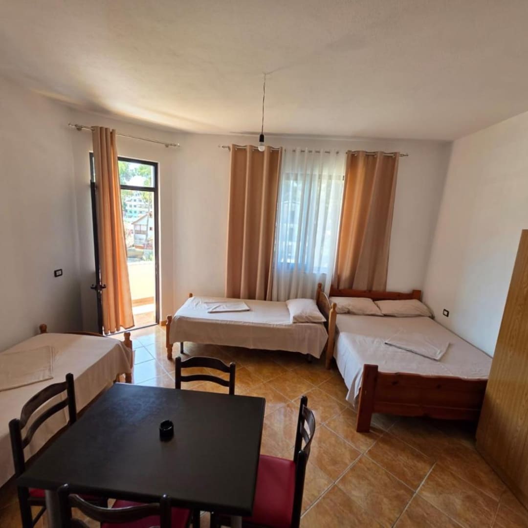 Three beds, a dining table and a wardrobe in a tiled room, with the balcony door open