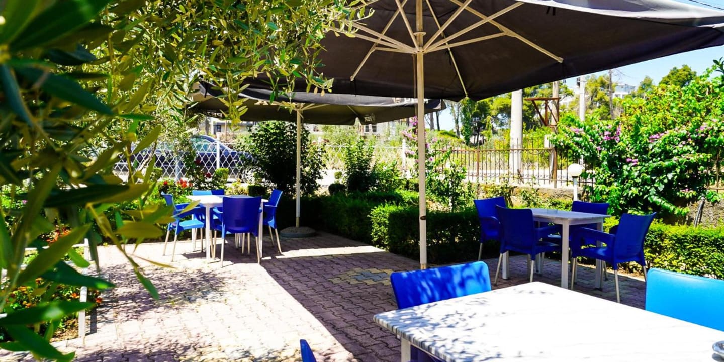 Tables and blue chairs under parasols on the garden terrace, with hedges and flowers around