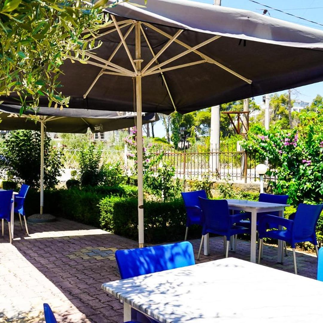Tables and blue chairs under parasols on the garden terrace, with hedges and flowers around