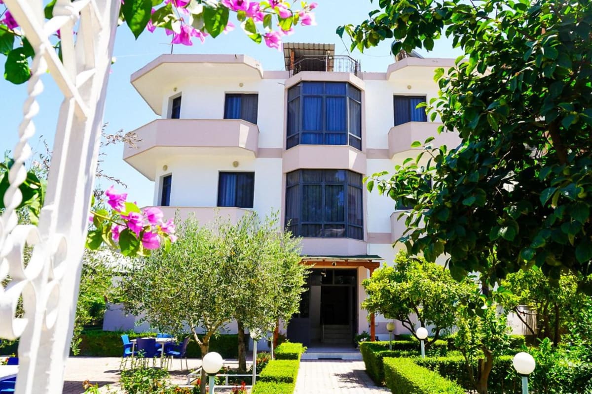 The villa seen from its garden: balconies above olive trees, a hedged path to the door and pink bougainvillea