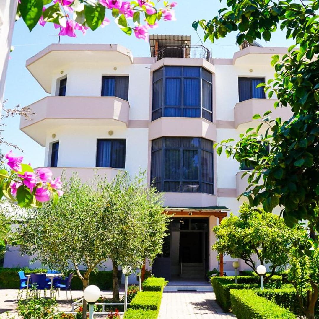 The villa seen from its garden: balconies above olive trees, a hedged path to the door and pink bougainvillea